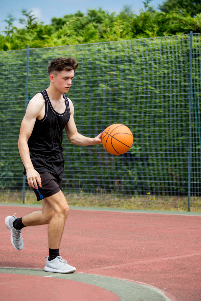 Хлопчик-підліток підстрибує у баскетбол на дворі
 - Фото, зображення