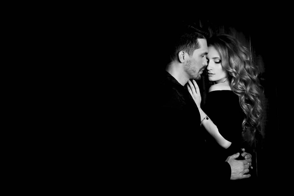 Beautiful couple in love hugging against black background. Studio black and white portrait photo of a girl blondes and a guy with short hair. Valentine's day. Loving married couple. Family happiness. - Photo, Image