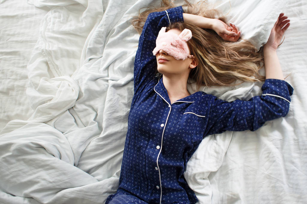 Loira bonito em sua cama em pijama azul e máscara de sono, vista superior
 - Foto, Imagem