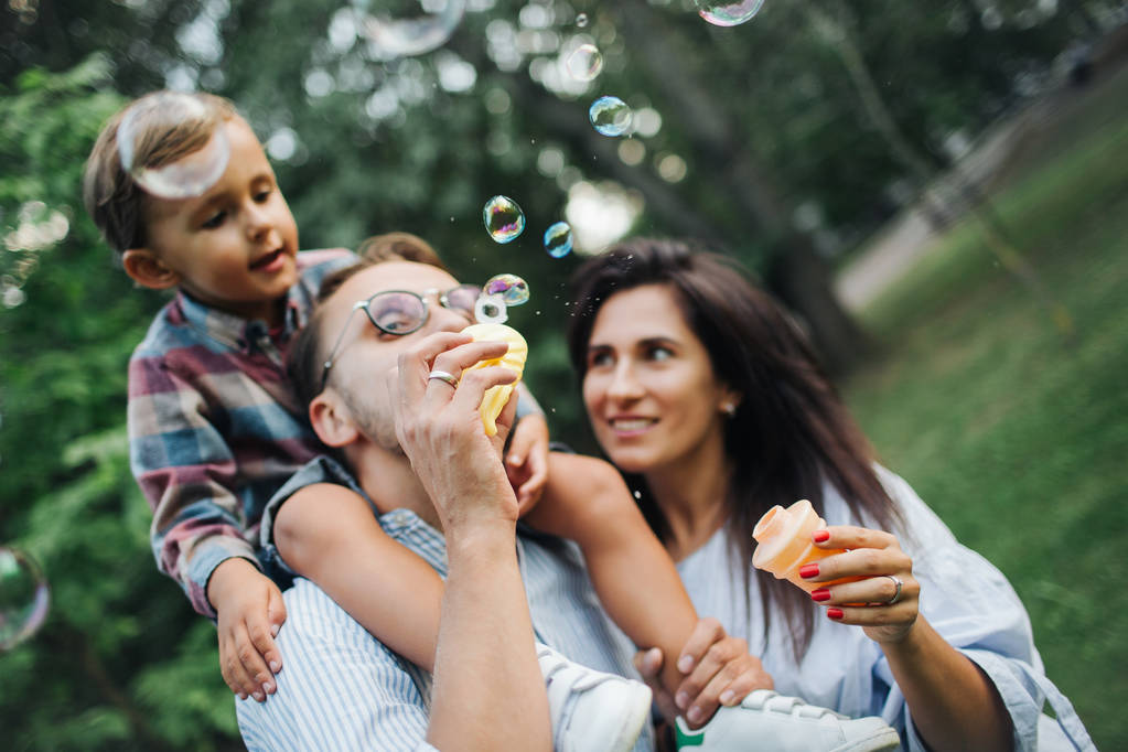 Счастливая молодая семья играет с мыльными палочками в парке на открытом воздухе
 - Фото, изображение