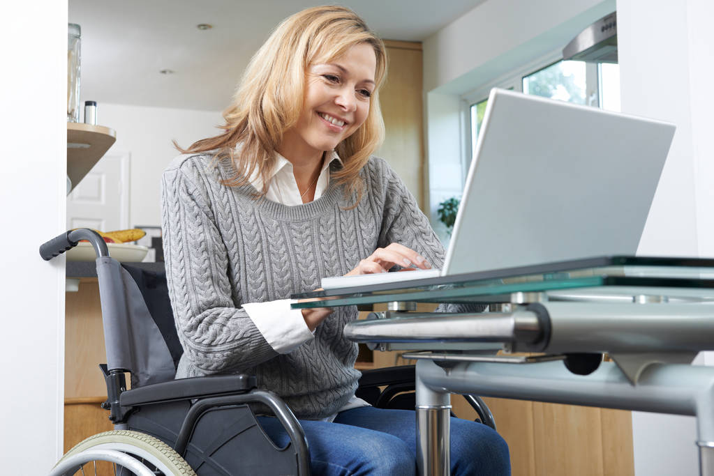 Behinderte Frau im Rollstuhl benutzt Laptop zu Hause - Foto, Bild