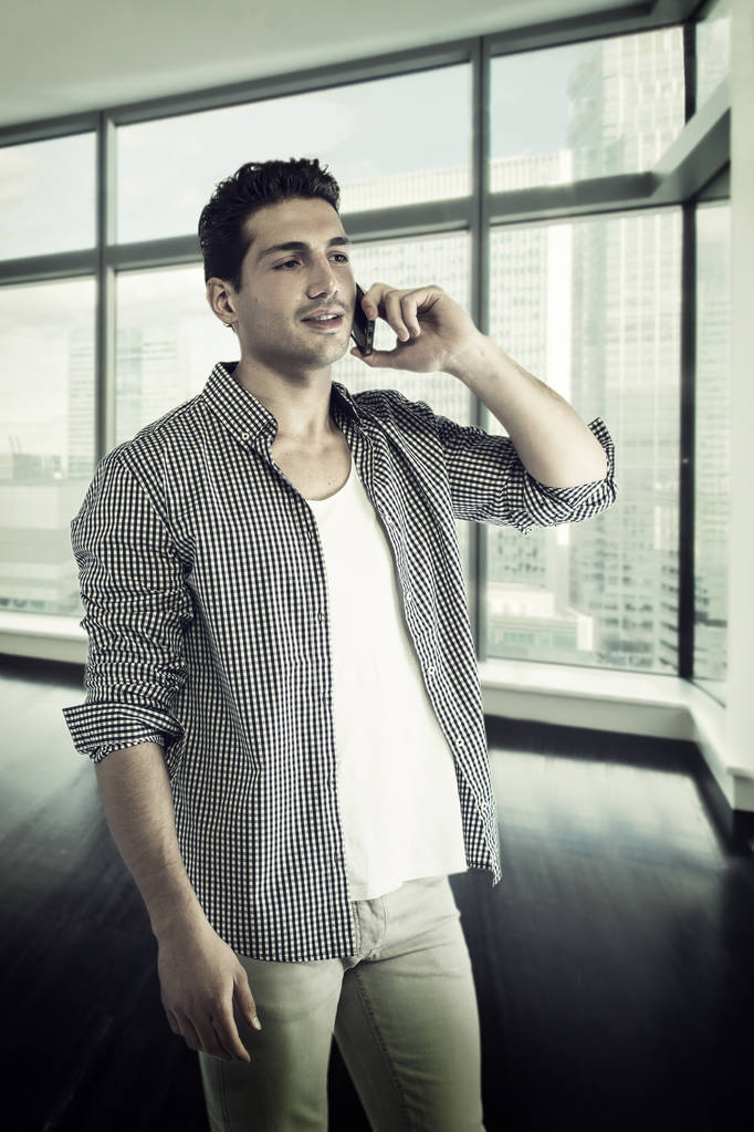 Красивий молодий чоловік розмовляє по мобільному телефону, посміхаючись
 - Фото, зображення