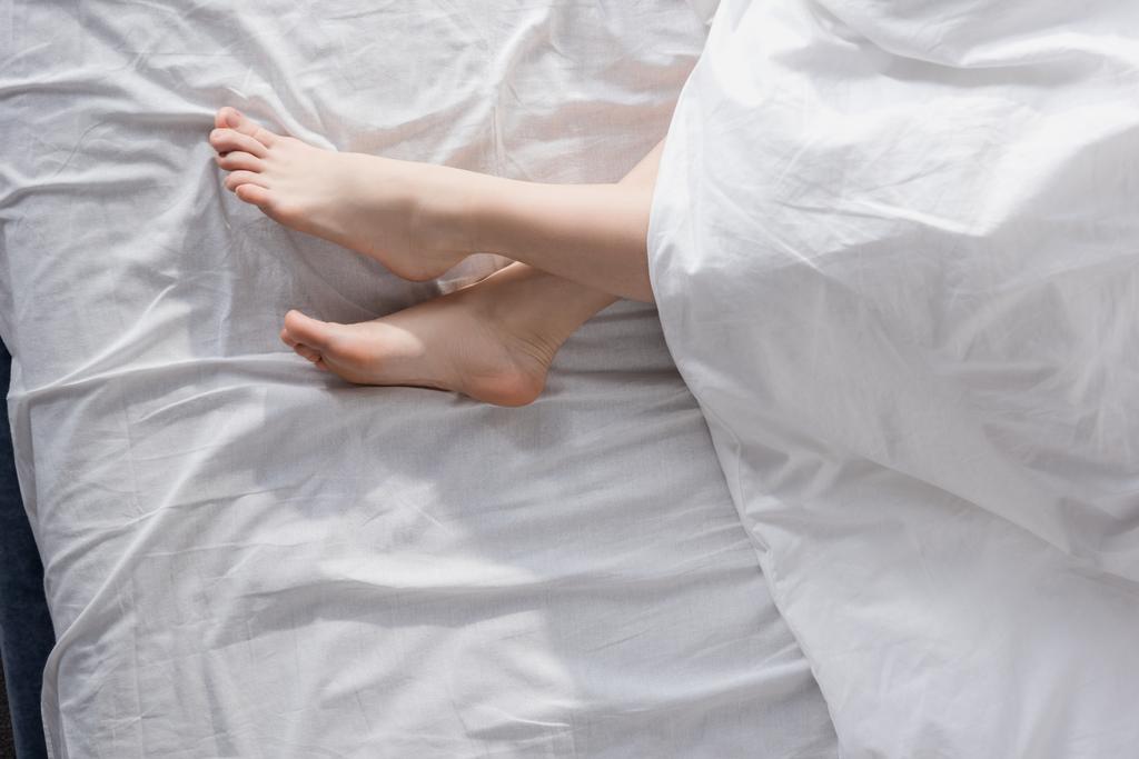 pés femininos que se estendem fora do cobertor
 - Foto, Imagem