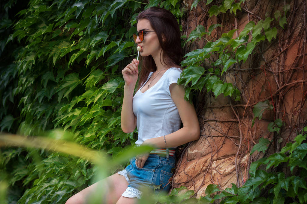 Urocza brunetka z okularami pozowanie w parku, w pobliżu liści - Zdjęcie, obraz