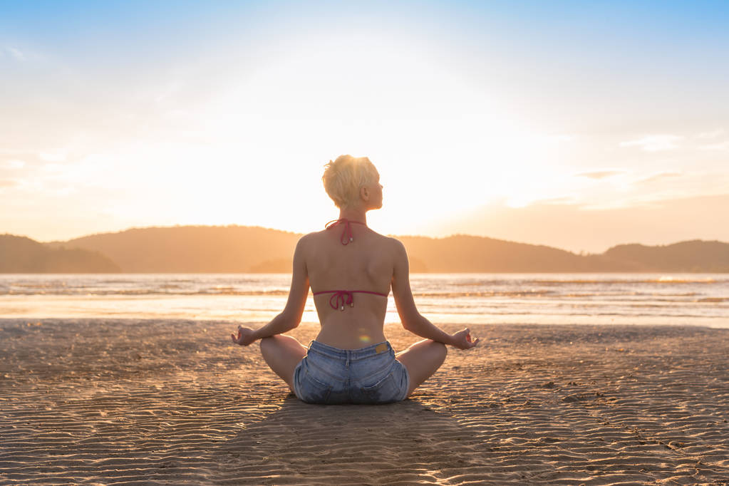夕日、美しい女性の練習ヨガ夏休み瞑想海辺のビーチにロータス ポーズを座っている若い女の子 - 写真・画像