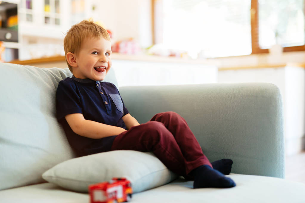 Onnellinen poika istuu sohvalla olohuoneessa
 - Valokuva, kuva