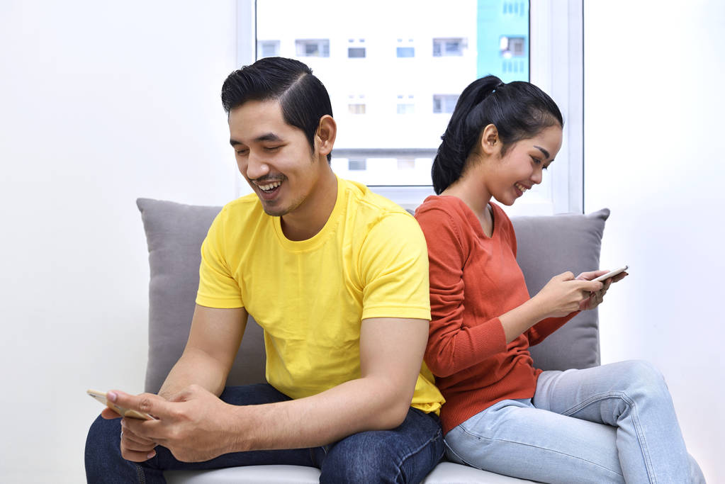 Coppia asiatica seduta con telefoni cellulari
 - Foto, immagini