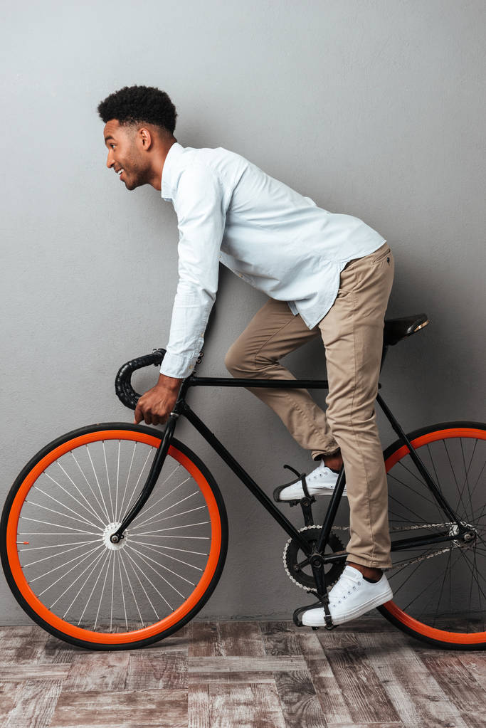 Jonge Afrikaanse man permanent over grijs muur met fiets. - Foto, afbeelding