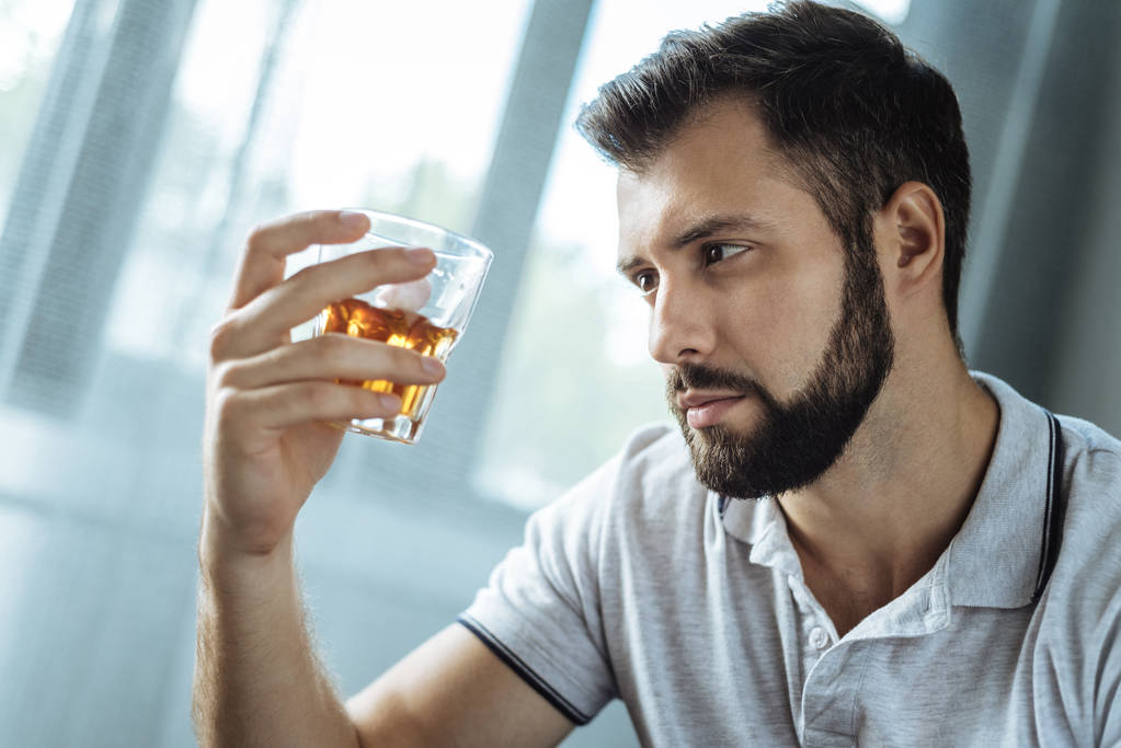 Ζοφερός εθισμένος άνδρα να κρατάει ένα ποτήρι με ουίσκι - Φωτογραφία, εικόνα