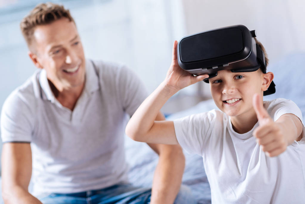 Niño feliz usando auriculares VR y mostrando los pulgares hacia arriba
 - Foto, Imagen