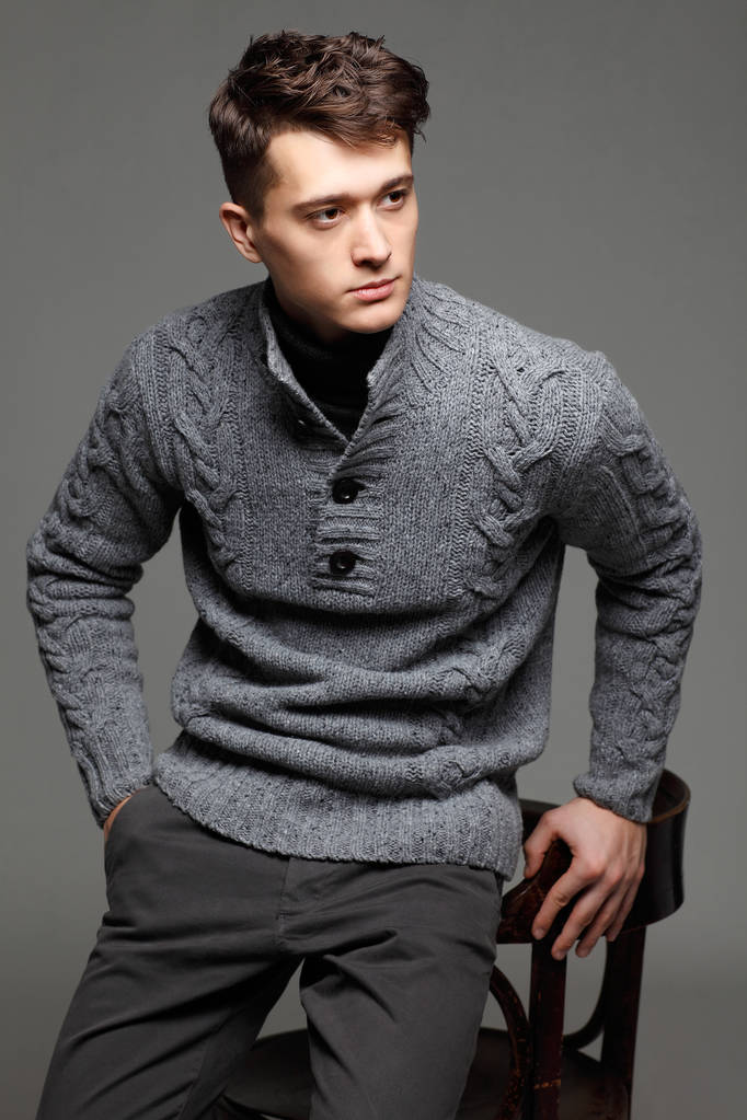 sexy junger Mann in warmem Strickpulli vor grauem Hintergrund. männliches Modell.  - Foto, Bild
