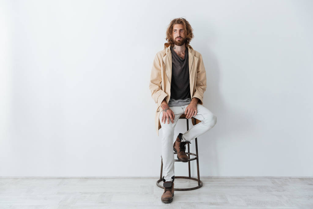 Caucasian young bearded man sitting isolated over grey wall - Photo, Image
