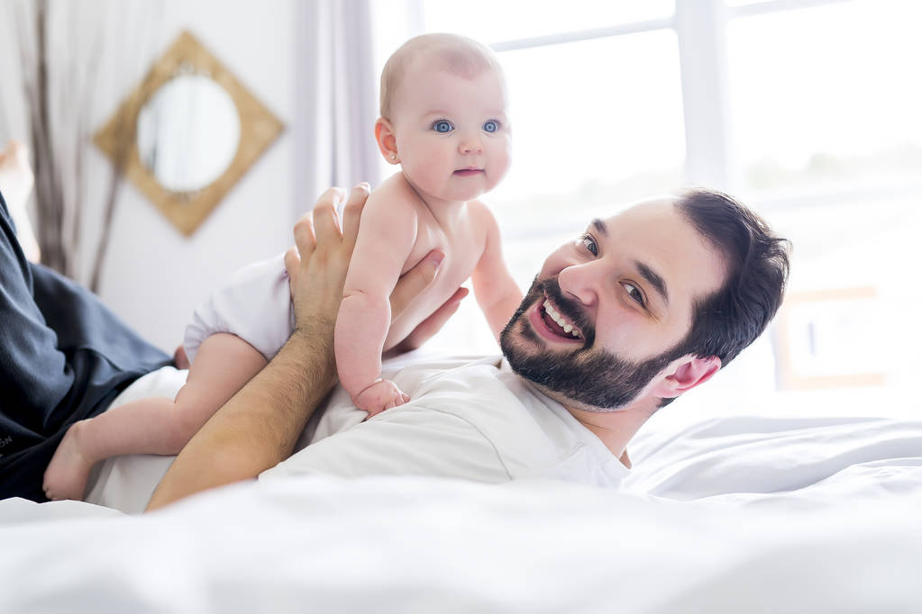 Młody szczęśliwy ojciec bawiący się łóżeczkiem - Zdjęcie, obraz