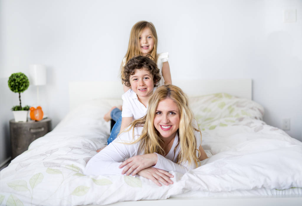Портрет счастливой матери и ее детей, лежащих на кровати
 - Фото, изображение