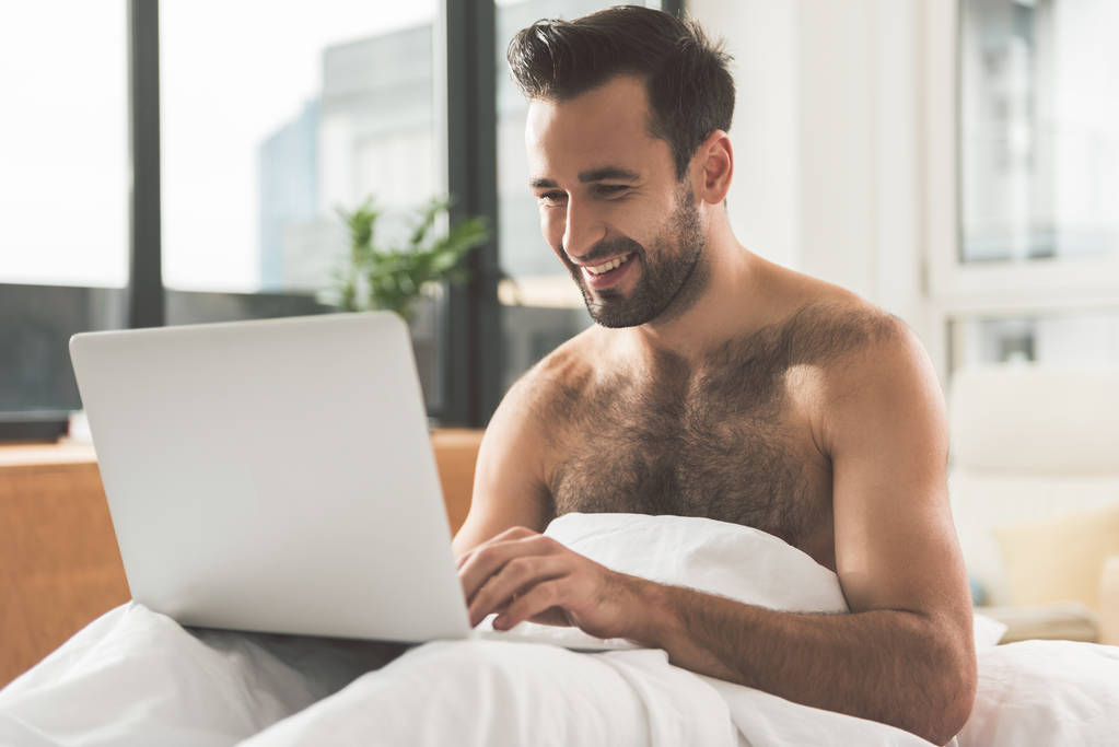 glücklicher Mann mit modernem Computer im Bett - Foto, Bild