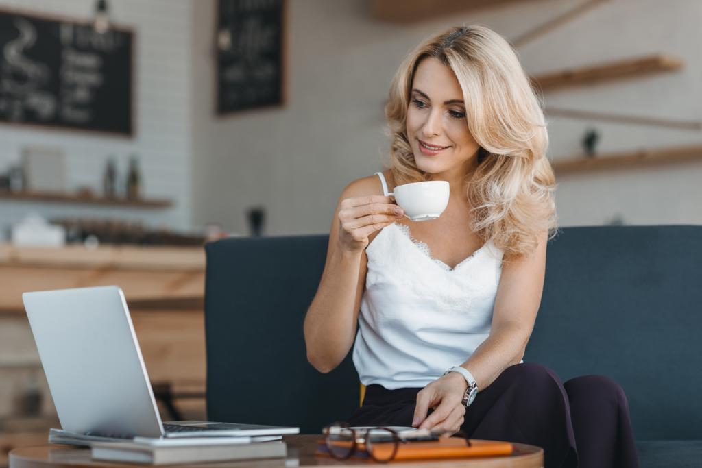 Donna che beve caffè e utilizza computer portatile
 - Foto, immagini