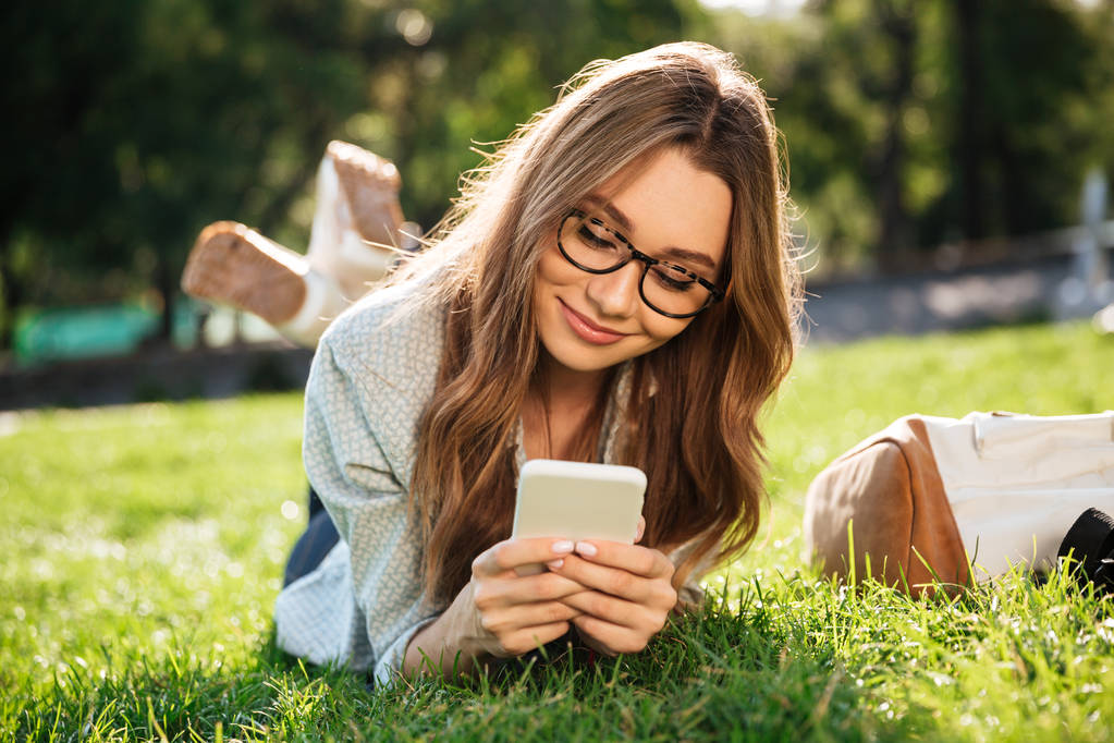 Blij brunette vrouw in brillen liggen op gras - Foto, afbeelding