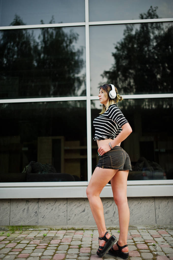 Menina desgaste em shorts com fones de ouvido grandes contra grandes janelas bu
 - Foto, Imagem