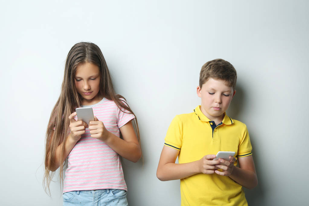 Νεαρό αγόρι και κορίτσι με smartphones σε γκρίζο φόντο - Φωτογραφία, εικόνα