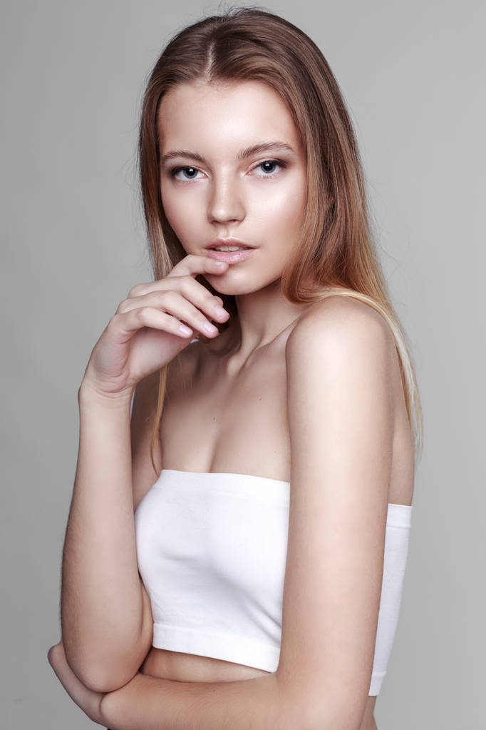 Modeporträt eines Mädchens posiert in hellem, geräumigem Studio mit grauem Hintergrund in stilvoller, bequemer und einfacher Kleidung. junges Mädchen mit sauberer Haut und perfektem Gesicht  - Foto, Bild