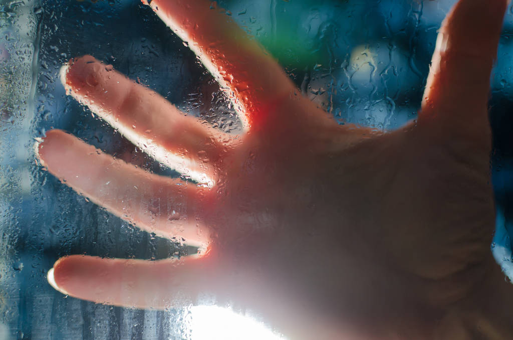 Mans mão no fundo da luz brilhante através do vidro molhado
 - Foto, Imagem