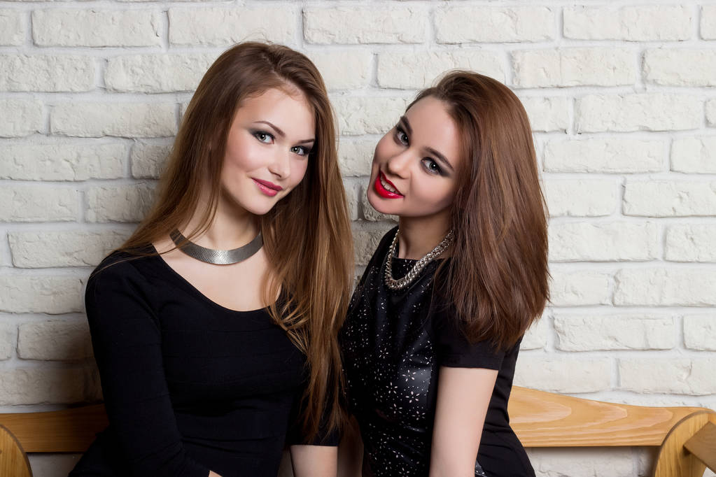 zwei schöne junge Mädchen in schwarzen Kleidern sitzen auf der Bank und tratschen - Foto, Bild
