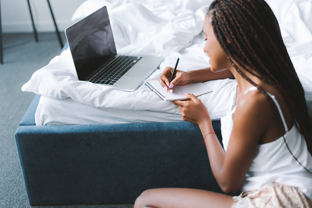 mujer con portátil en la cama escritura en bloc de notas
 - Foto, imagen