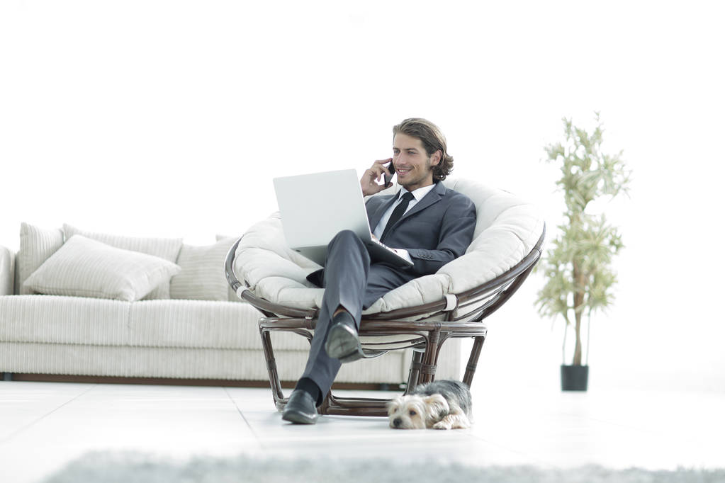 бизнесмен разговаривает по смартфону, сидя в гостиной
 - Фото, изображение