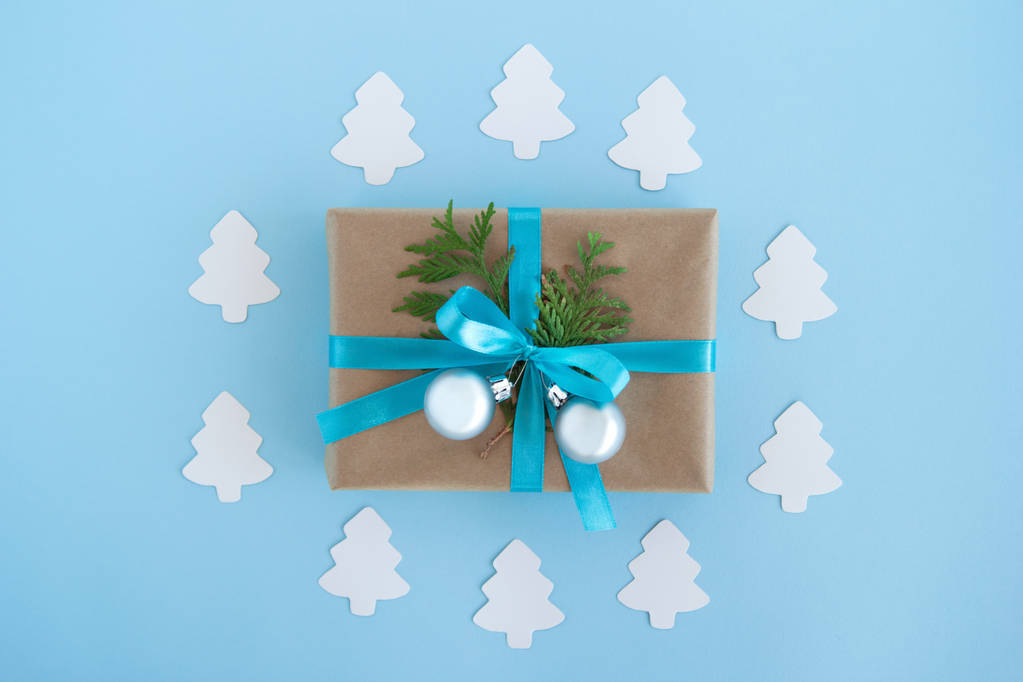 Luxe-geschenketui van Kraft papier, blauw lint gewikkeld en ingerichte fir takken en zilveren kerstballen op de blauwe achtergrond met papier fir tree, bovenaanzicht. - Foto, afbeelding