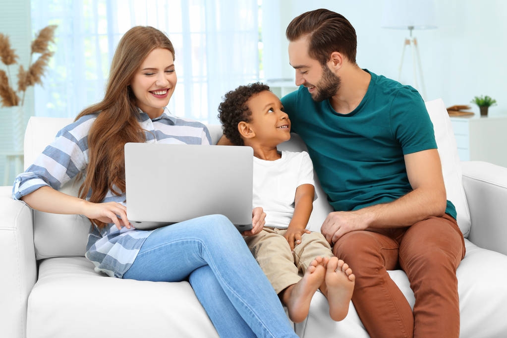 Couple heureux avec adopté afro-américain garçon en utilisant un ordinateur portable tout en étant assis sur le canapé à la maison
 - Photo, image