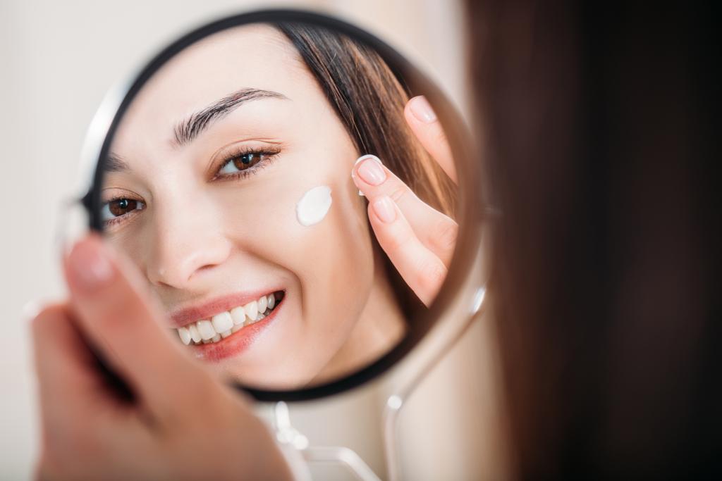 Mulher sorridente aplicando creme facial
 - Foto, Imagem