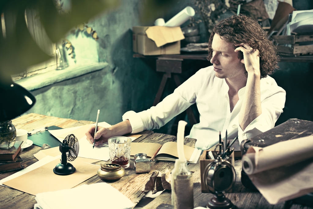 Spisovatel v práci. Pohledný mladý spisovatel sedí u stolu a psaní v jeho skicák - Fotografie, Obrázek