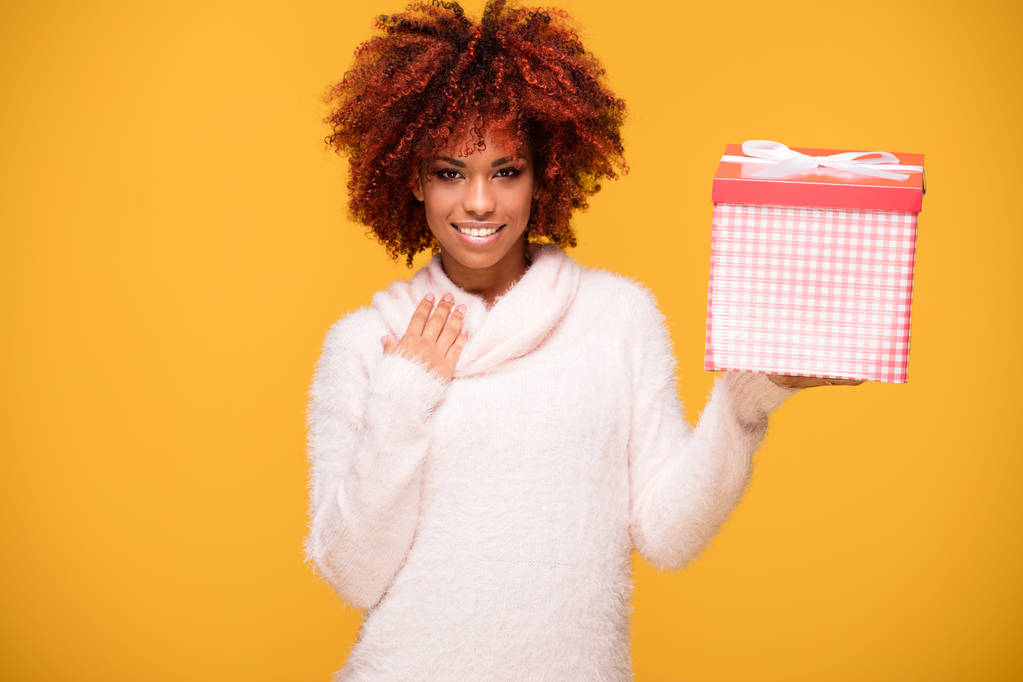 Αφρο κοπέλα ποζάρει με κιβώτιο δώρων, χαμογελώντας. - Φωτογραφία, εικόνα