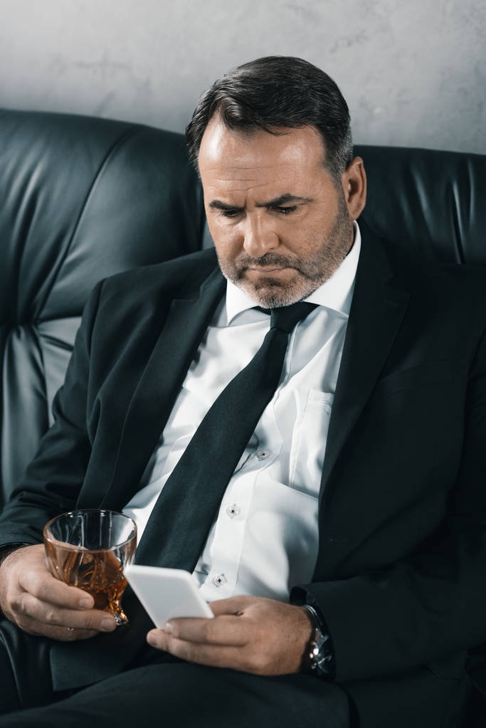 zakenman met glas whiskey met smartphone - Foto, afbeelding