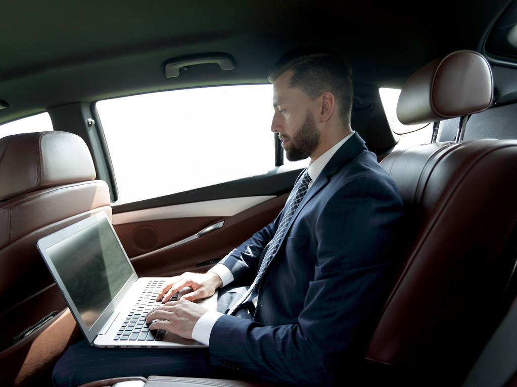 bir arabanın arka koltuğunda bir dizüstü bilgisayar kullanarak iş adamı - Fotoğraf, Görsel