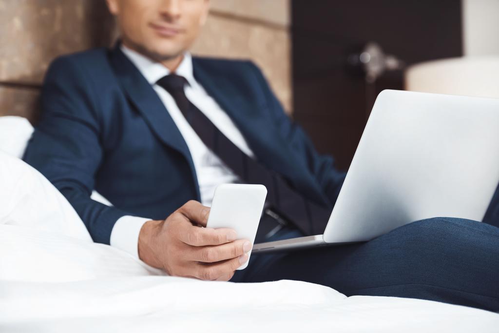 Üzletember ágyon a telefon és a laptop - Fotó, kép
