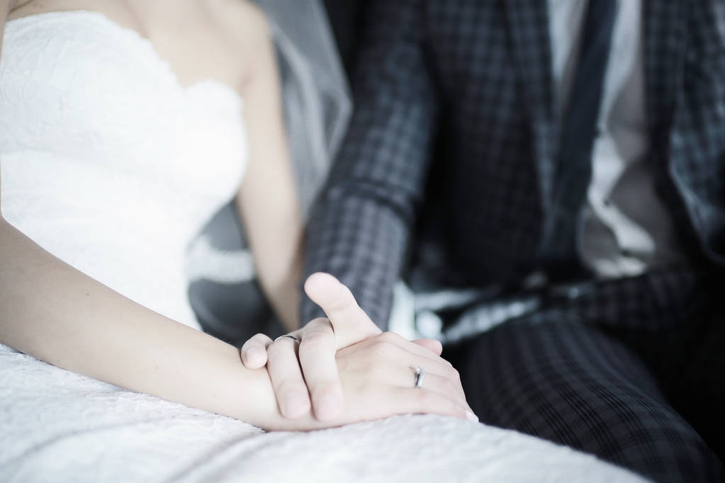 junge Braut in weißem Kleid und Bräutigam sitzen zusammen und halten Händchen am Hochzeitstag  - Foto, Bild