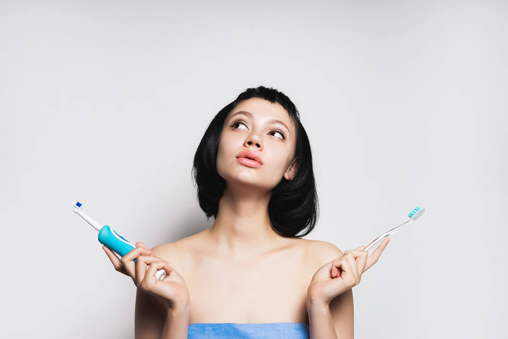 chica con el pelo negro corto después de una ducha elige qué cepillo para cepillarse los dientes
 - Foto, imagen
