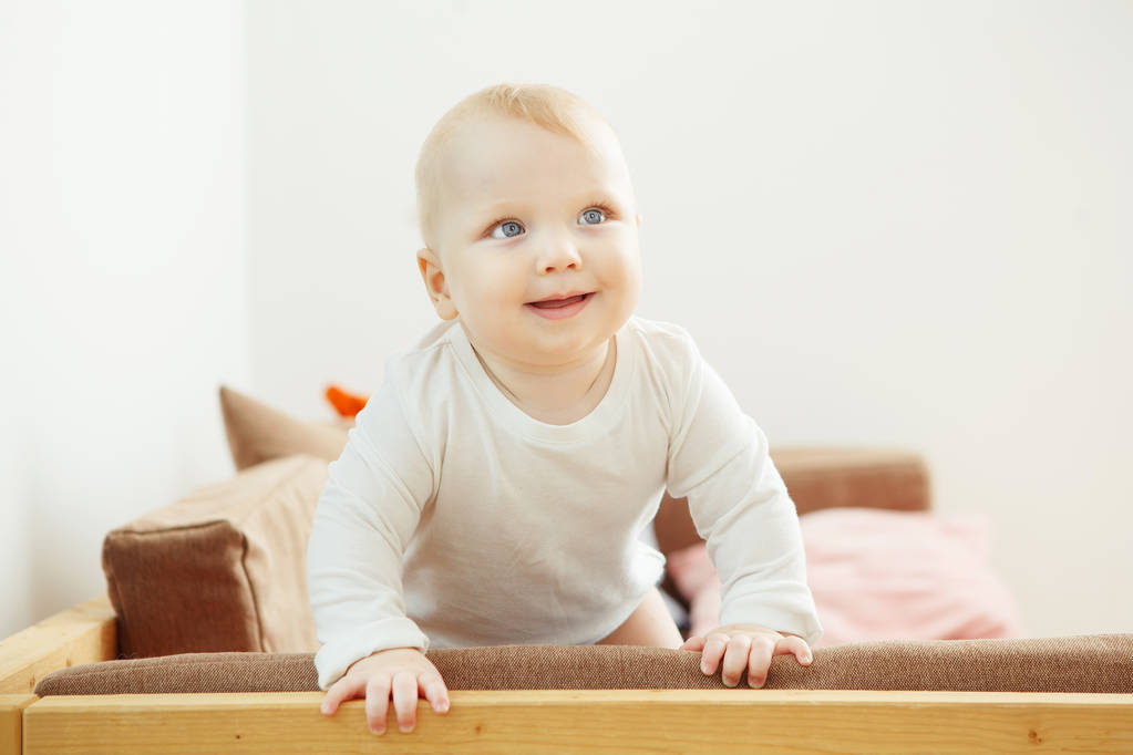 Χαμογελώντας μωρό στέκεται στο καναπέ στηριζόμενη στην υποστήριξη. - Φωτογραφία, εικόνα