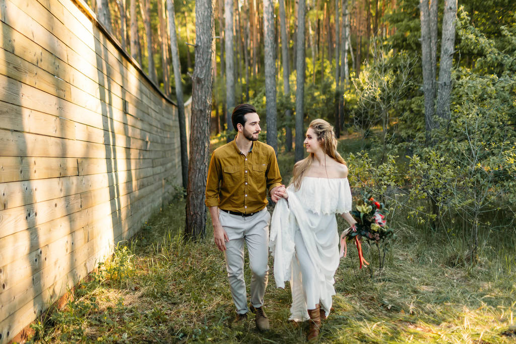 Νεόνυμφοι είναι το περπάτημα στο δάσος. Κορίτσι σε λευκό φόρεμα και ο άνθρωπος σε ένα πουκάμισο ελιάς. Ρουστίκ γάμου. Έργα τέχνης. - Φωτογραφία, εικόνα