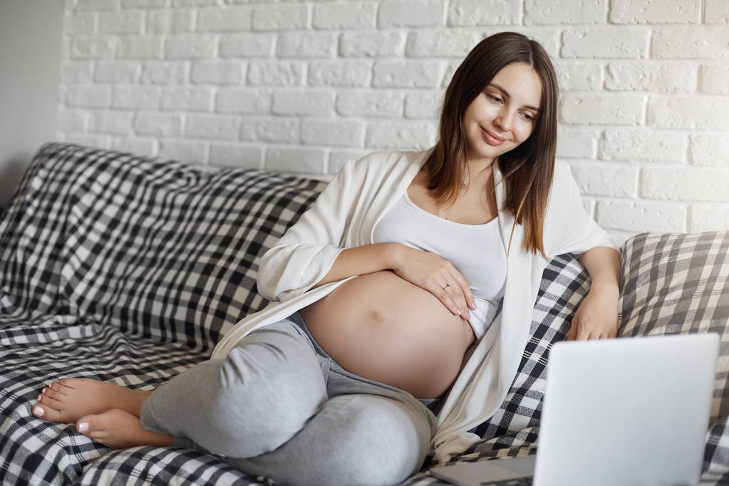 Belle dame enceinte en bonne santé se détendre sur le canapé regarder de nouvelles vidéos populaires chat en ligne. La grossesse est relaxante
. - Photo, image