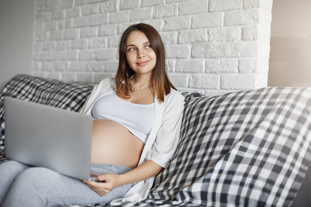 Madre joven usando un ordenador portátil para planear su regreso a la actividad física. El embarazo es un buen momento para renovar la casa
. - Foto, Imagen