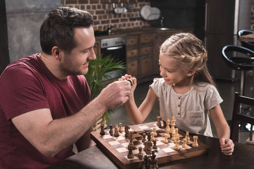 Isä ja tytär törmäävät shakkinappuloihin
 - Valokuva, kuva