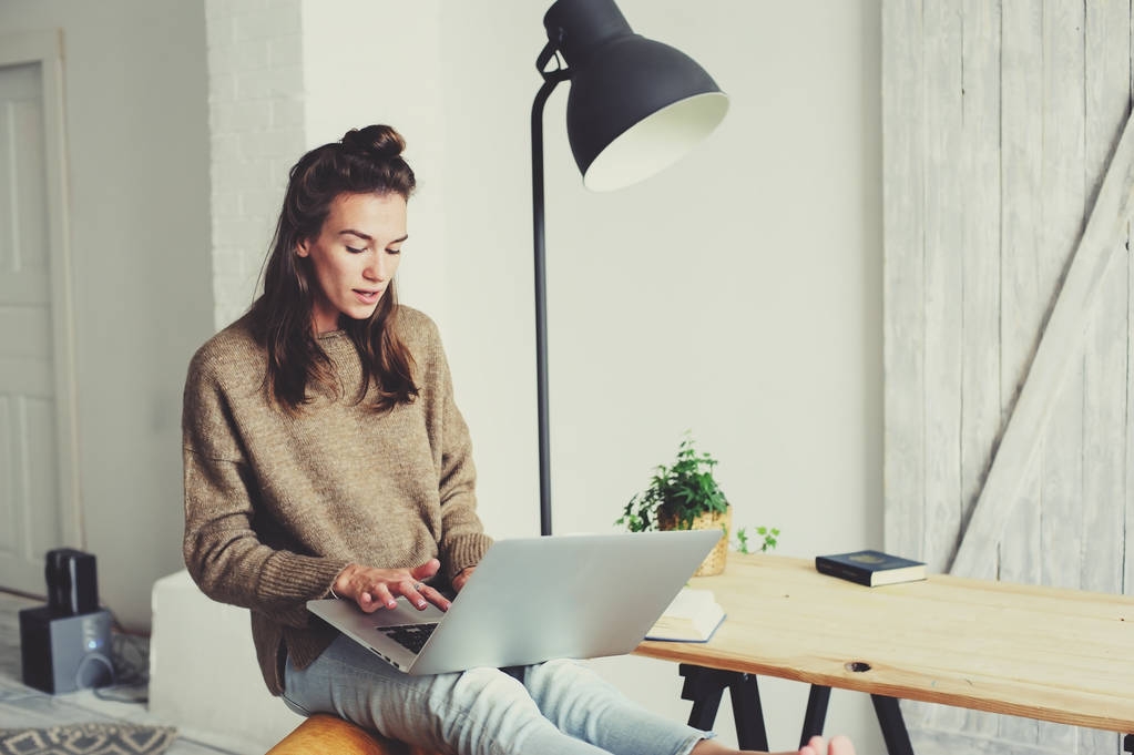 jovem mulher bonita compras em casa on-line com laptop e xícara de café pela manhã. Home office no interior escandinavo moderno
 - Foto, Imagem
