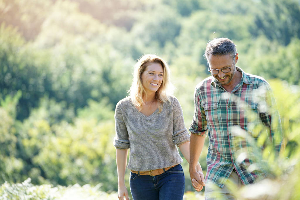 Happy mature couple walking in countryside on sunny day - Photo, Image