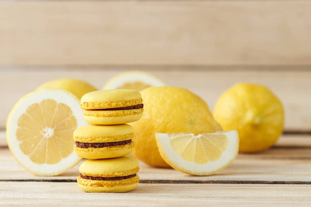Gele Franse macarons met citroenen op het houten bord - Foto, afbeelding