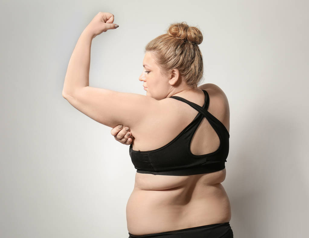 Mujer tocando grasa en su brazo contra fondo claro. Concepto de pérdida de peso
 - Foto, Imagen