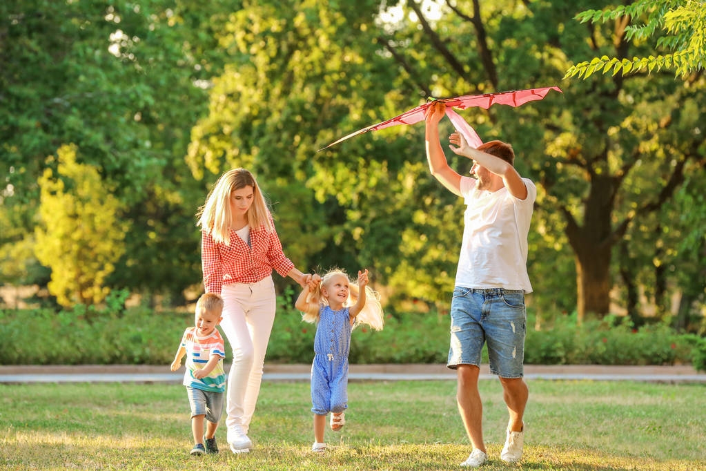 glückliche Familie spielt mit Drachen im Park an sonnigem Tag - Foto, Bild