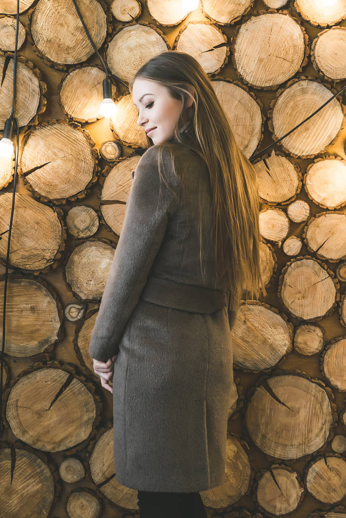 красивая молодая девушка в длинной блузке, стоящая у необычной стены
 - Фото, изображение