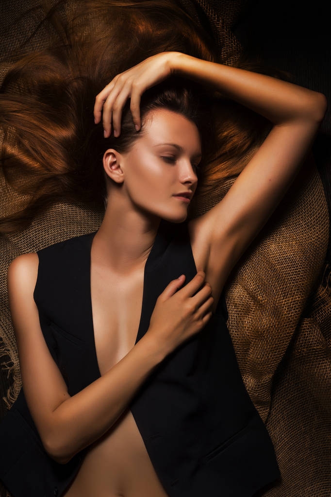 naakte sensuele vrouw in unbuttoned vest ligt op jute weefsel - Foto, afbeelding
